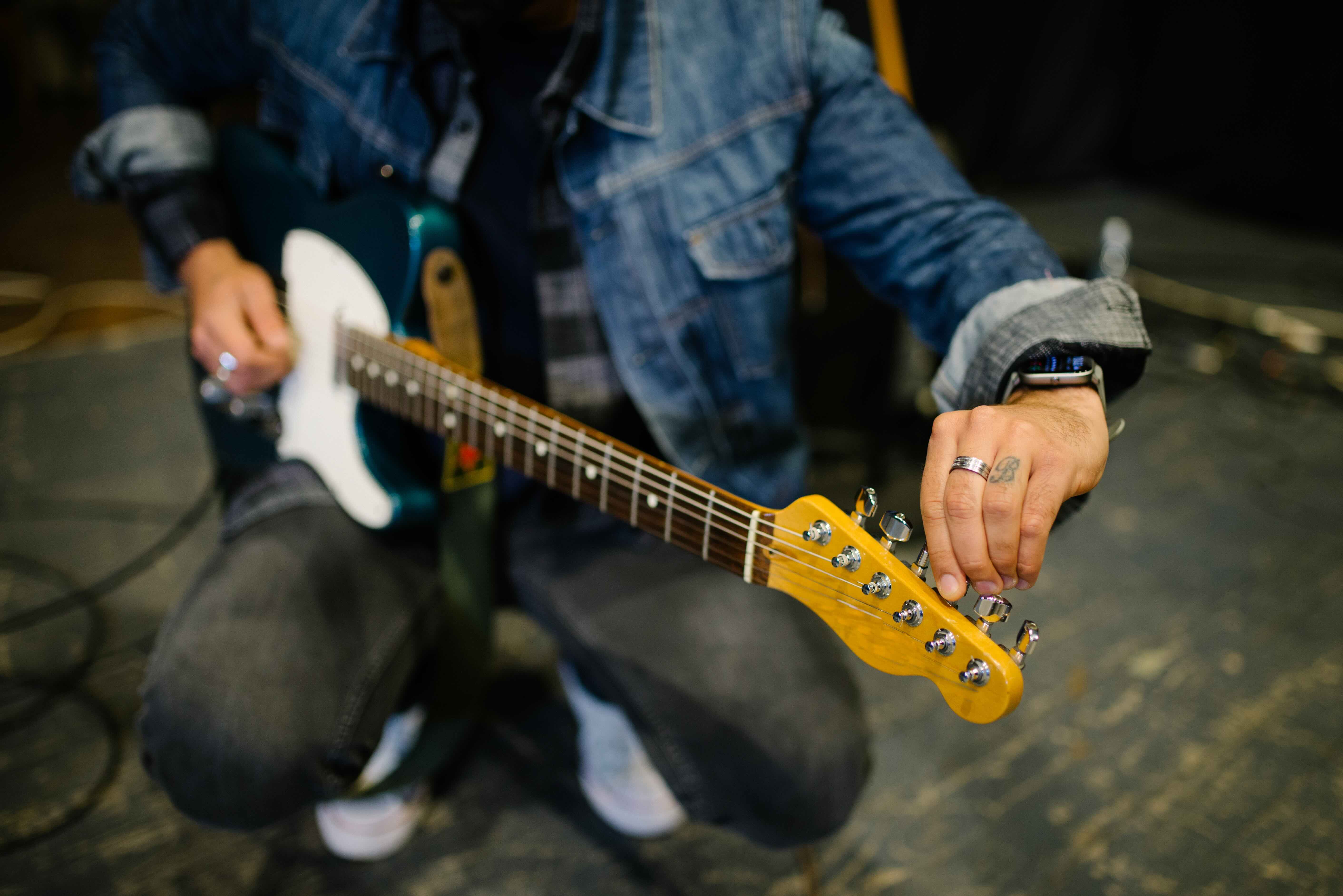 Gitarrist i jeansjacka stämmer sin gitarr