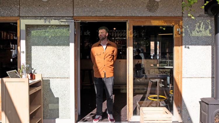 En man I orange skjorta står i öppningen till en resturang
