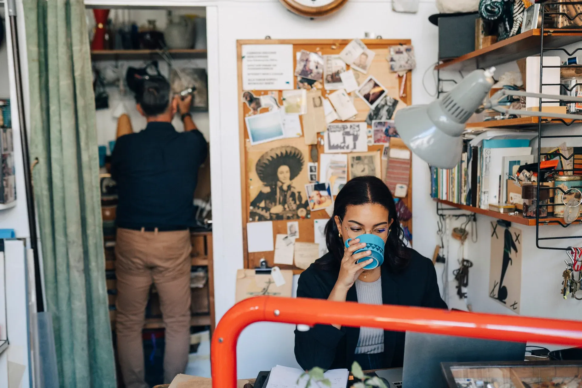 Kvinna dricker kaffe på rörigt, kreativt kontor